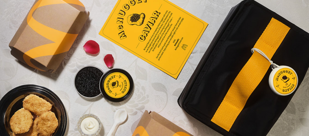 Boxes with McNugget caviar-themed labels, containers of caviar, nuggets on a plate, a yellow brochure, and a black bag. Tablecloth with floral pattern.